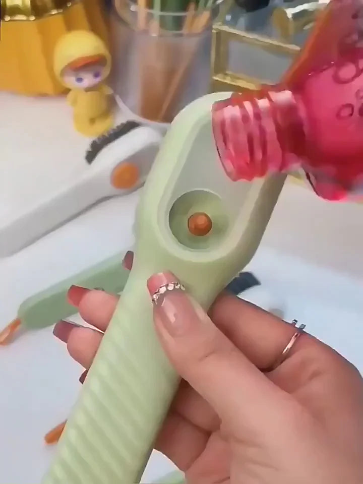 Hand holding a green tool with a pink nozzle, surrounded by various items on a surface.